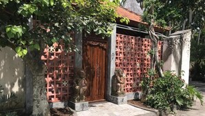 A traditional house with a wooden door, a red lattice wall, and two stone statues. - Akatara Hotel (Penida Island)