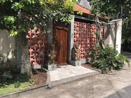 Una casa tradicional con puerta de madera, pared de celosía roja y dos estatuas de piedra.