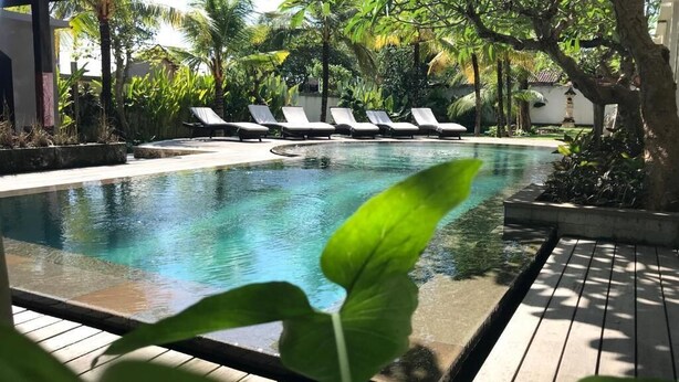 A swimming pool with lounge chairs, surrounded by tropical plants and a wooden deck. - Akatara Hotel (Penida Island)