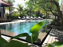 Una piscina con sillas de descanso, rodeada de plantas tropicales y una terraza de madera.
