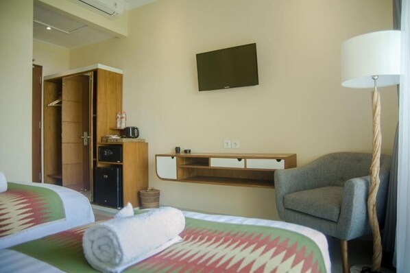 A hotel room with two beds, a TV on the wall, a desk with a lamp, and a wardrobe.