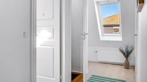 Une pièce avec une porte blanche, une fenêtre donnant sur un immeuble, un radiateur et un tapis à rayures vertes.