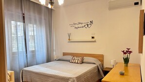 A neatly arranged bedroom with a bed, a bedside table with a vase of flowers, a wall-mounted shelf, and a decorative sign. - VACATION HOUSE IN OSTIA LEVANTE WITH 6 BEDS - ADJACENT LIDO NORD STATION (Lido di Ostia)