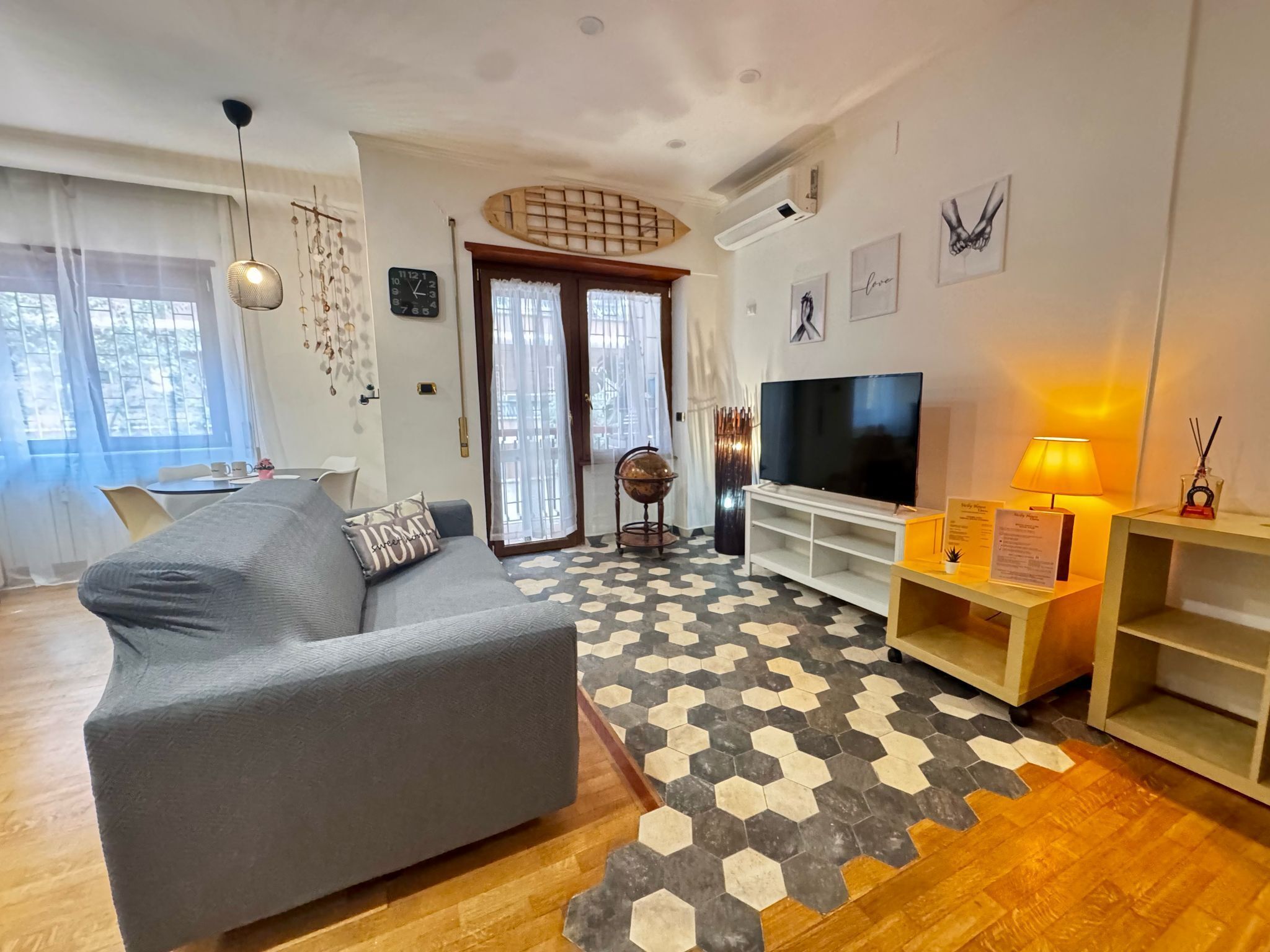 A modern living room with a grey sofa, a flat-screen TV, and a patterned rug.