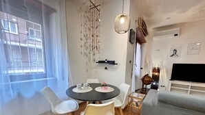 A modern living room with a round dining table, white chairs, a grey sofa, a flat-screen TV, and a decorative wall hanging. - VACATION HOUSE IN OSTIA LEVANTE WITH 6 BEDS - ADJACENT LIDO NORD STATION (Lido di Ostia)