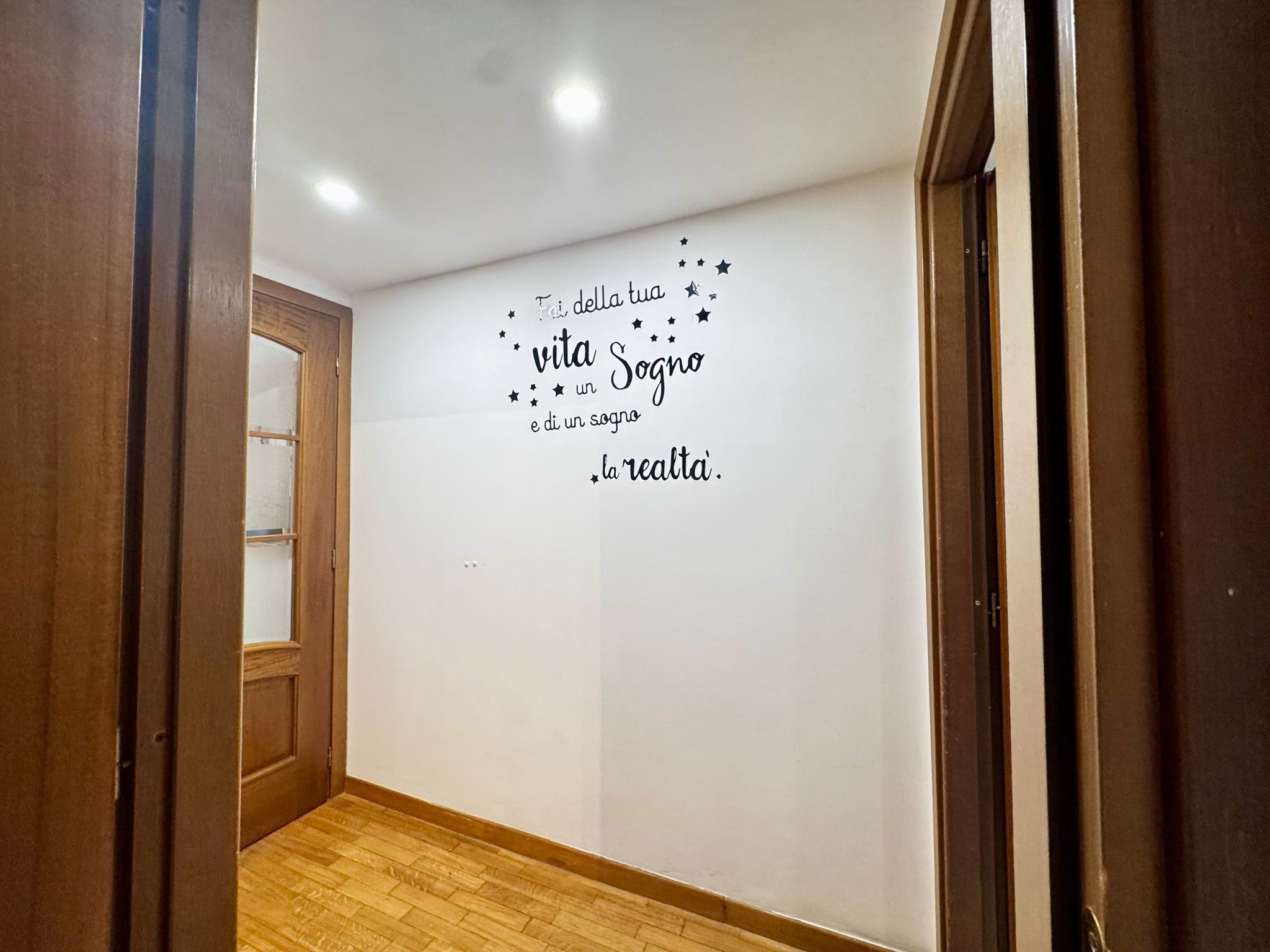 Un couloir doté d’un plancher en bois et d’un mur orné d’une citation inspirante en italien.