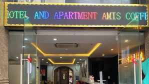 L’entrée d’un hôtel, avec une porte en verre, un comptoir de réception et une enseigne indiquant : « HÔTEL ET APPARTEMENTS AMIS COFFEE ».