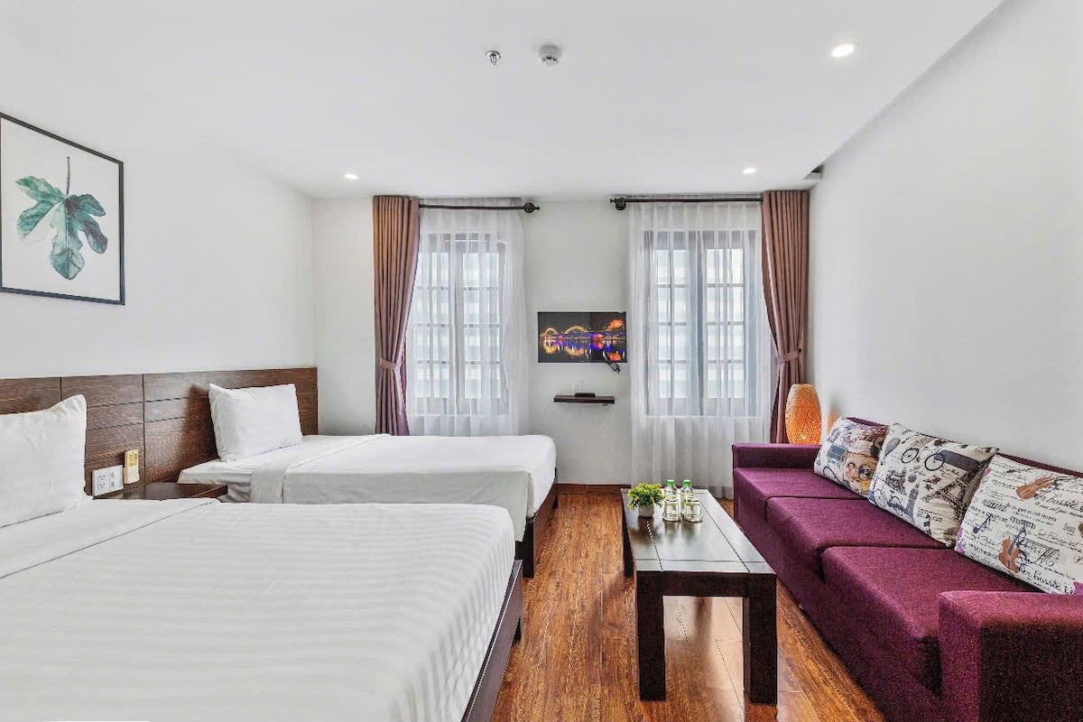 A hotel room with two beds, a sofa, a small table with decorative items, and a TV on the wall.