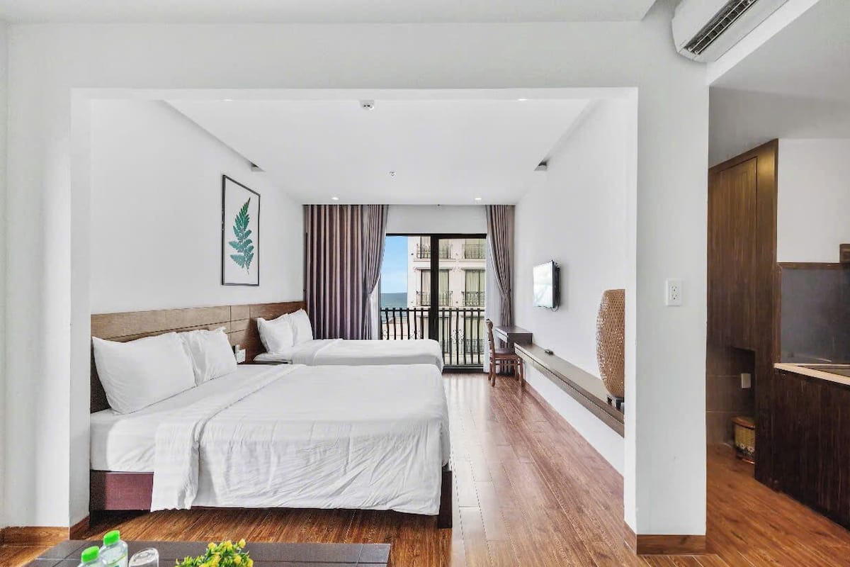 A hotel room with two beds, a TV, a balcony, and a wooden floor.