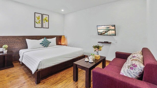 Una habitación de hotel con una cama, cabecera de madera, mesita de noche, mesa de centro, sofá y televisor montado en la pared.
