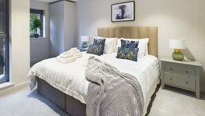 A modern bedroom with a large bed, bedside tables, a window, and a framed picture on the wall. - Wild Roses | The Rowan Retreat · Lake District (Backbarrow)