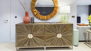 A wooden console with a sunburst design, a round mirror, a vase with branches, and a lamp. - Wild Roses | The Rowan Retreat · Lake District (Backbarrow)