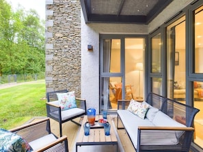 Une terrasse avec des meubles d’extérieur, un mur en pierre et de grandes fenêtres.