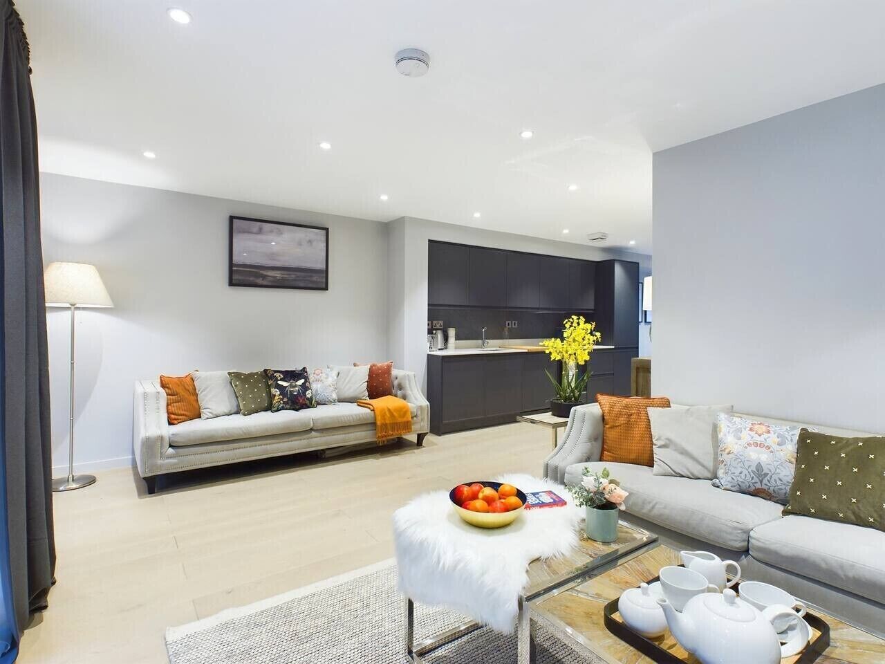 Uma sala de estar moderna com sofá, mesa de centro e área de cozinha ao fundo.