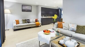 A modern living room with a sofa, coffee table, and a kitchen area in the background. - Wild Roses | The Rowan Retreat · Lake District (Backbarrow)