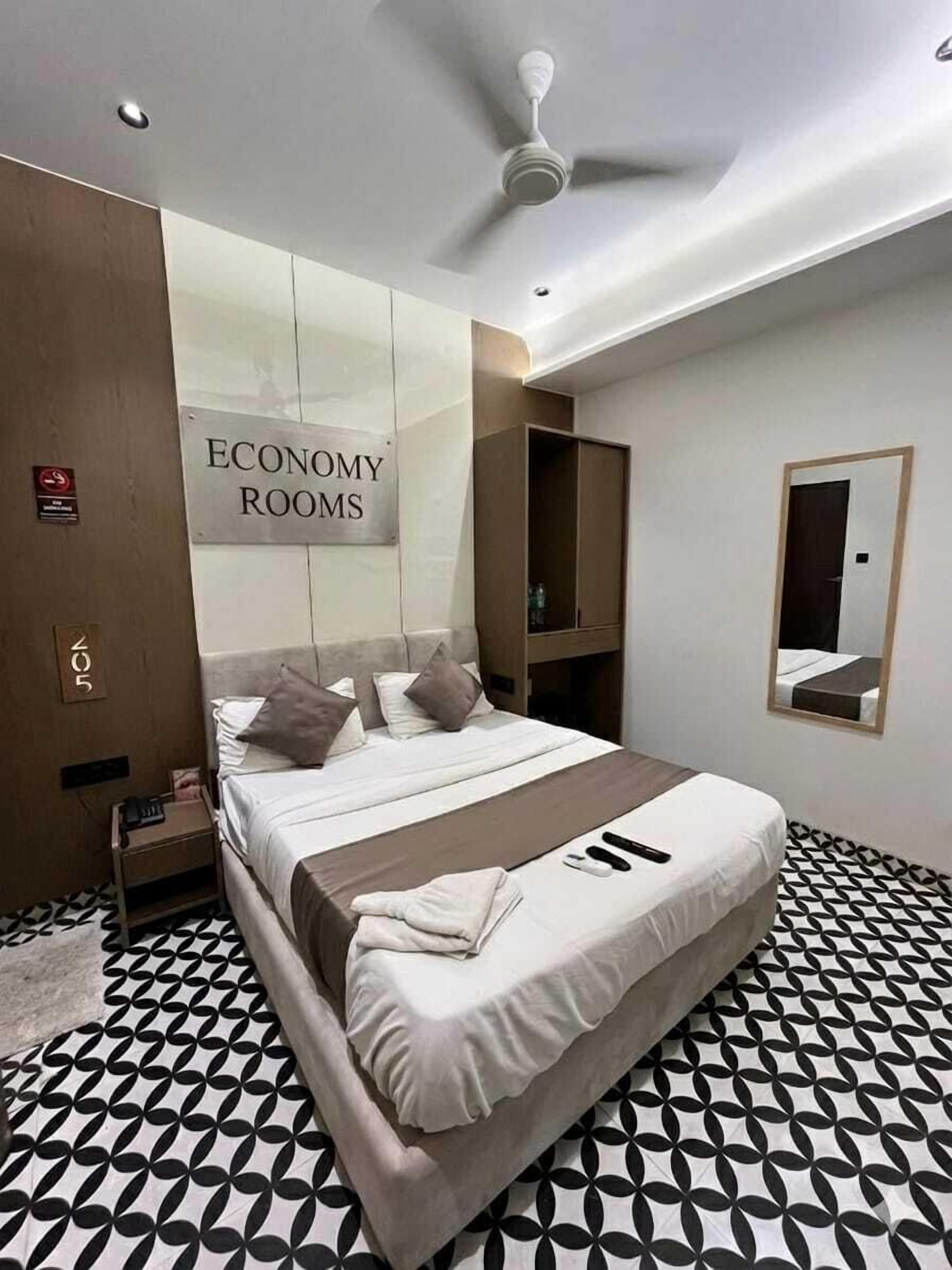 Habitación de hotel con cama, ventilador de techo, espejo y cartel que indica 'ECONOMY ROOMS'.