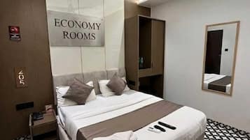 Habitación de hotel con cama, ventilador de techo, espejo y cartel que indica 'ECONOMY ROOMS'.