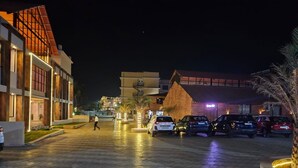 A parking area with multiple cars, a building with a sign reading "Omiya Jyoti School", and a well-lit walkway. - Hotel Prince Garden Daman (Daman)