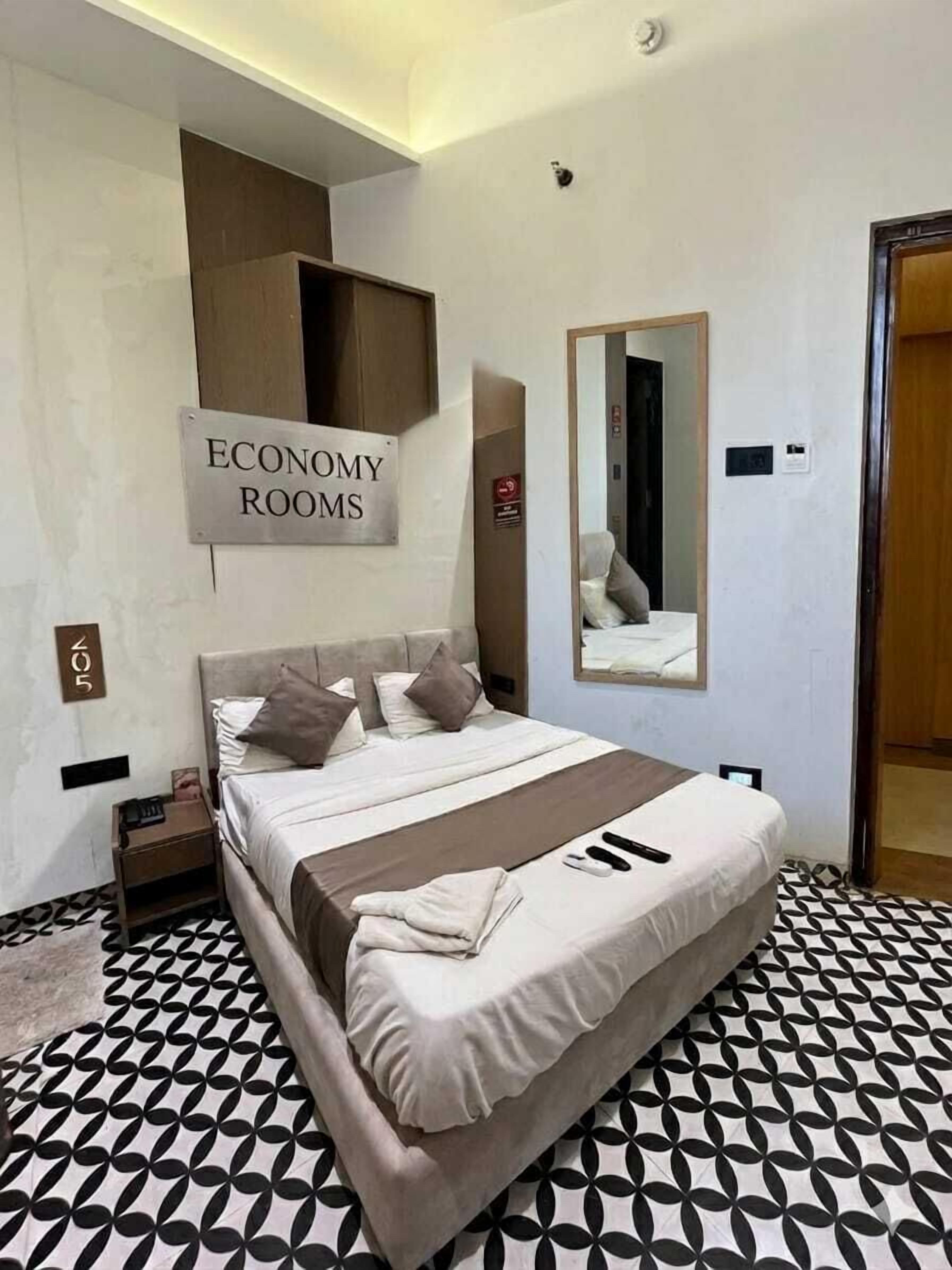 Un dormitorio con cama, almohadas, una mesita de noche, un espejo y un letrero que indica 'ECONOMY ROOMS'.