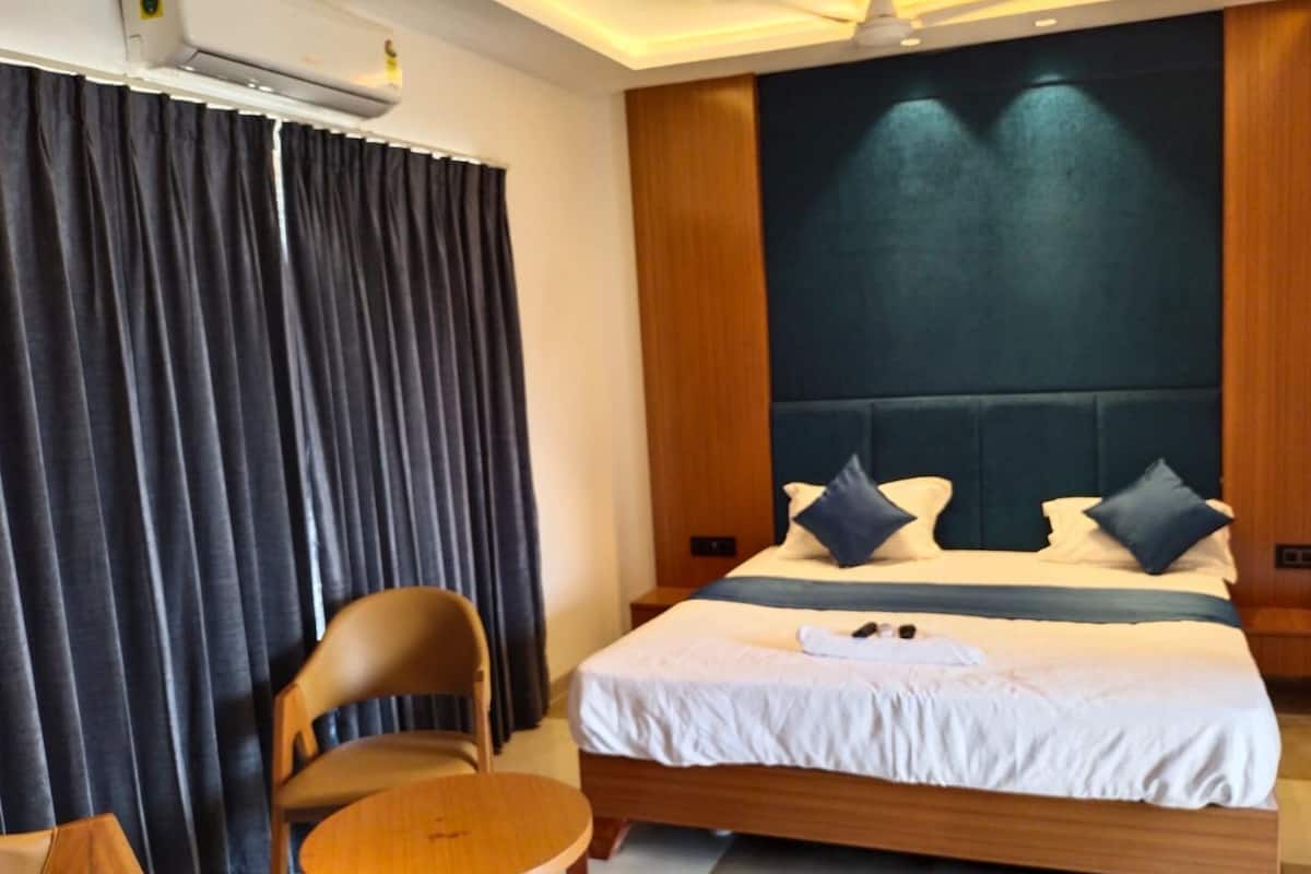 Une chambre d’hôtel avec un grand lit, des rideaux épais, une tête de lit en bois et une petite table ronde.