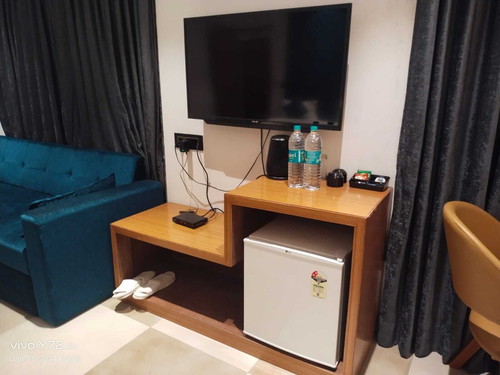 A compact room with a blue sofa, a small wooden table with a TV, a mini-fridge, and a pair of slippers on the floor.