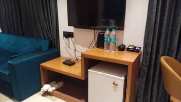 A compact room with a blue sofa, a small wooden table with a TV, a mini-fridge, and a pair of slippers on the floor.