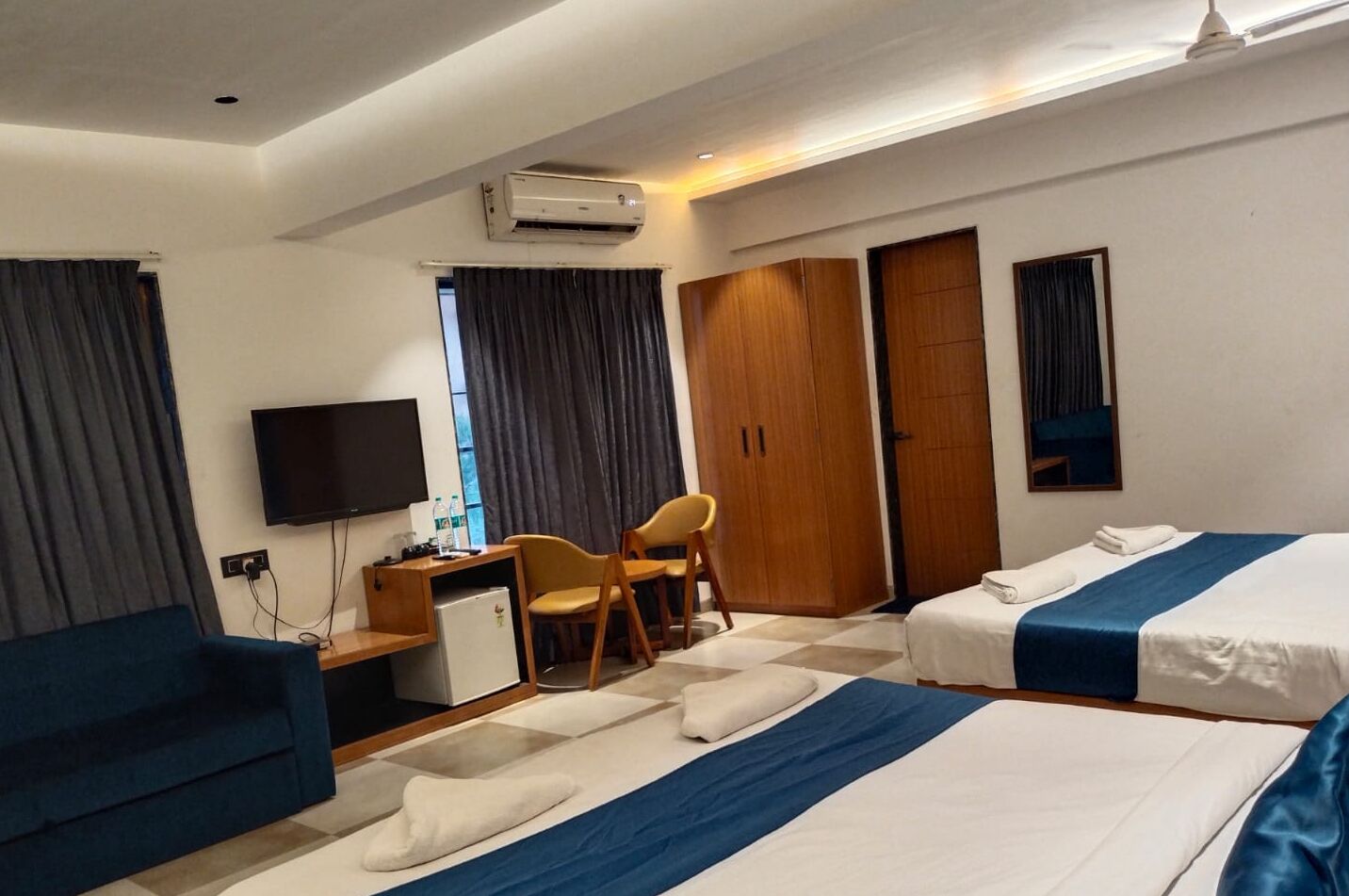 Una habitación de hotel con dos camas, un escritorio con silla, un televisor y un armario.