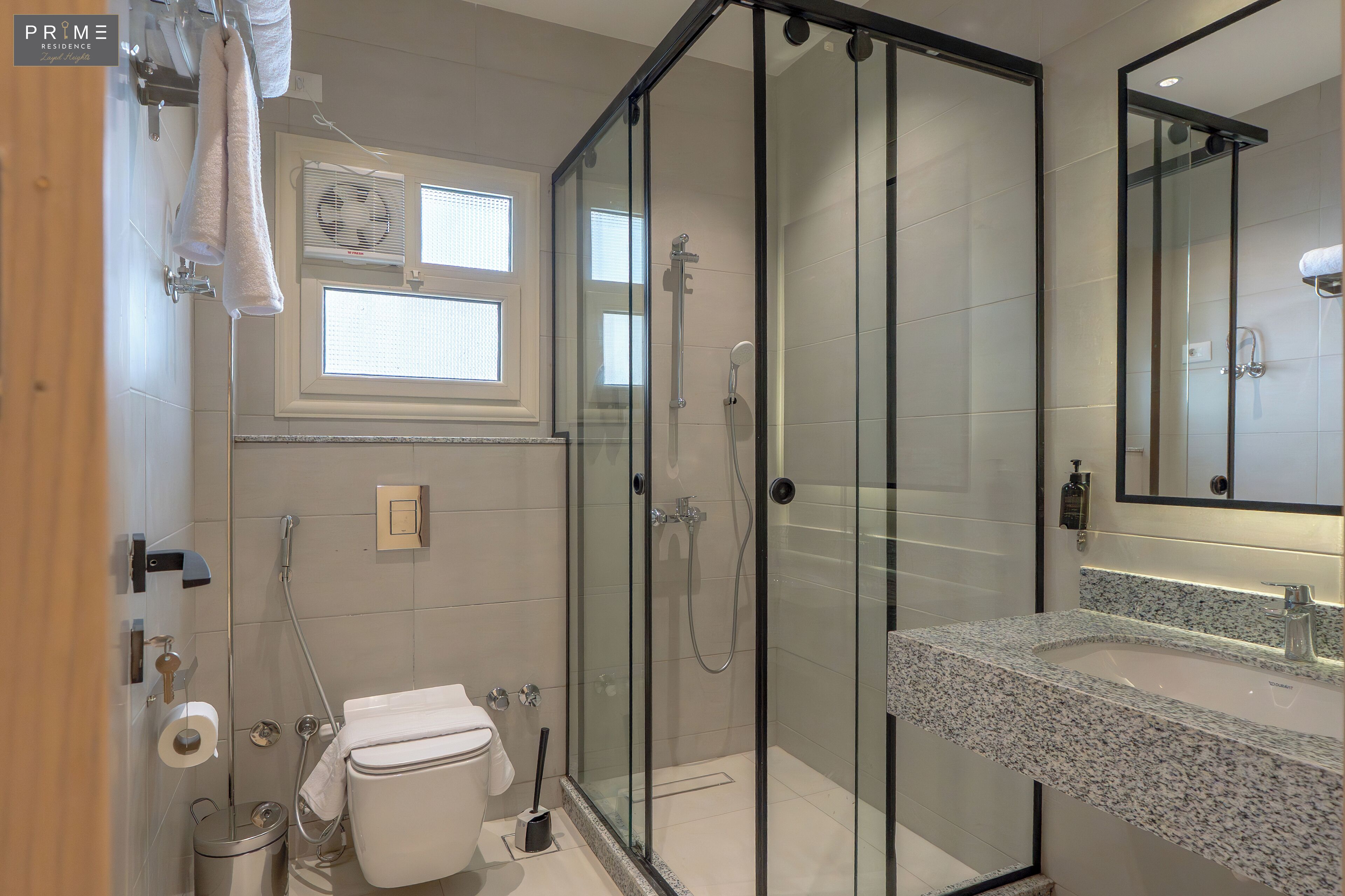 Une salle de bain moderne avec une douche à parois de verre, des toilettes blanches et un lavabo sur un plan de travail en granit.
