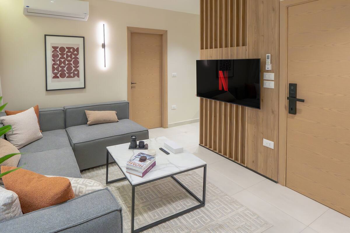 Ein modernes Wohnzimmer mit einem grauen Sofa, einem Couchtisch und einem Flachbildfernseher, der an einer Holzwand angebracht ist.