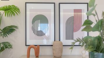 A modern interior with two framed abstract artworks, a glass-top table with decorative items, and green plants.