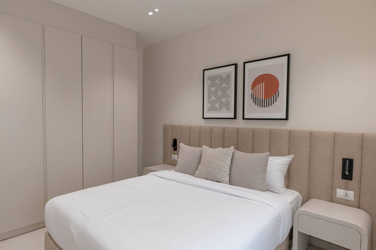 Ein modernes Schlafzimmer mit einem großen Bett, einem Kleiderschrank und zwei gerahmten Kunstwerken an der Wand.