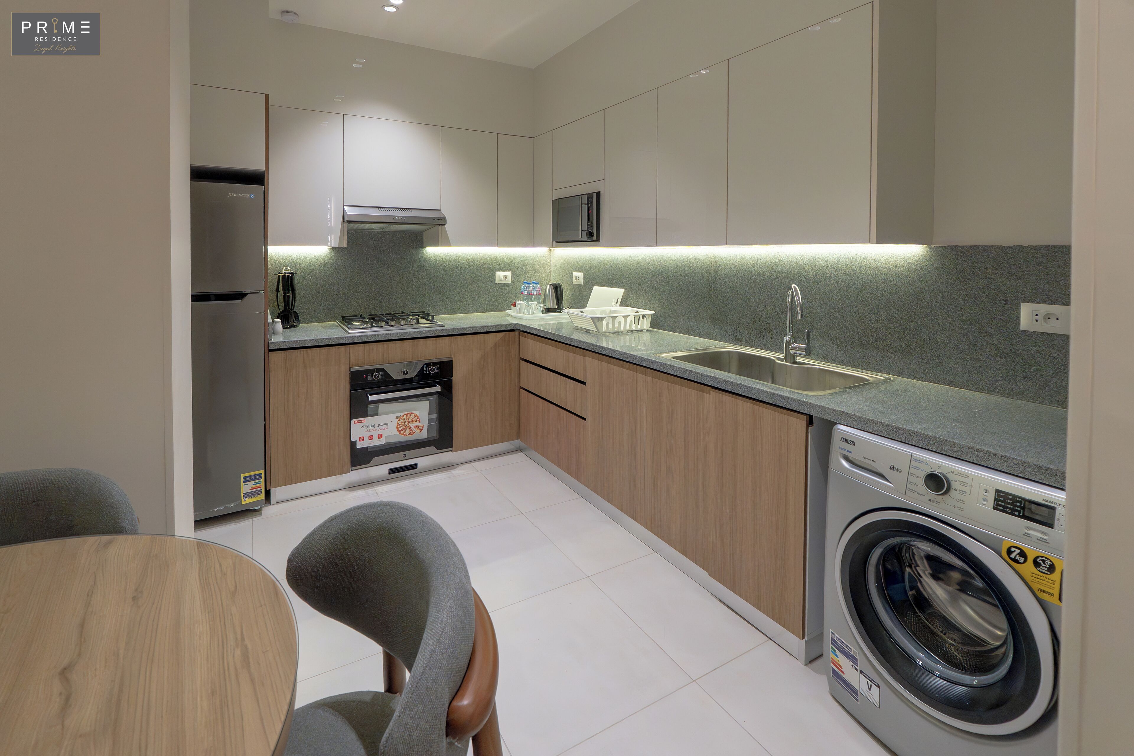 A modern kitchen with a built-in washing machine, a microwave, and a stainless steel refrigerator.