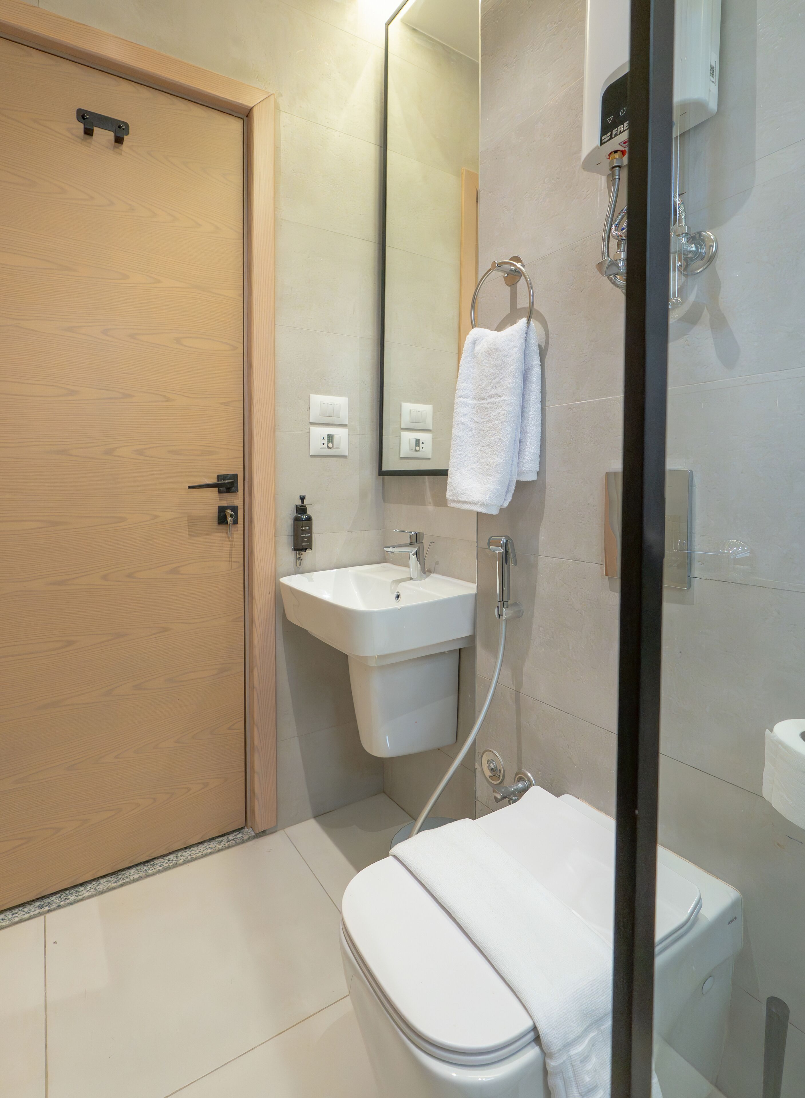 Un baño moderno con puerta de madera, lavamanos blanco, espejo y cabina de ducha de vidrio.