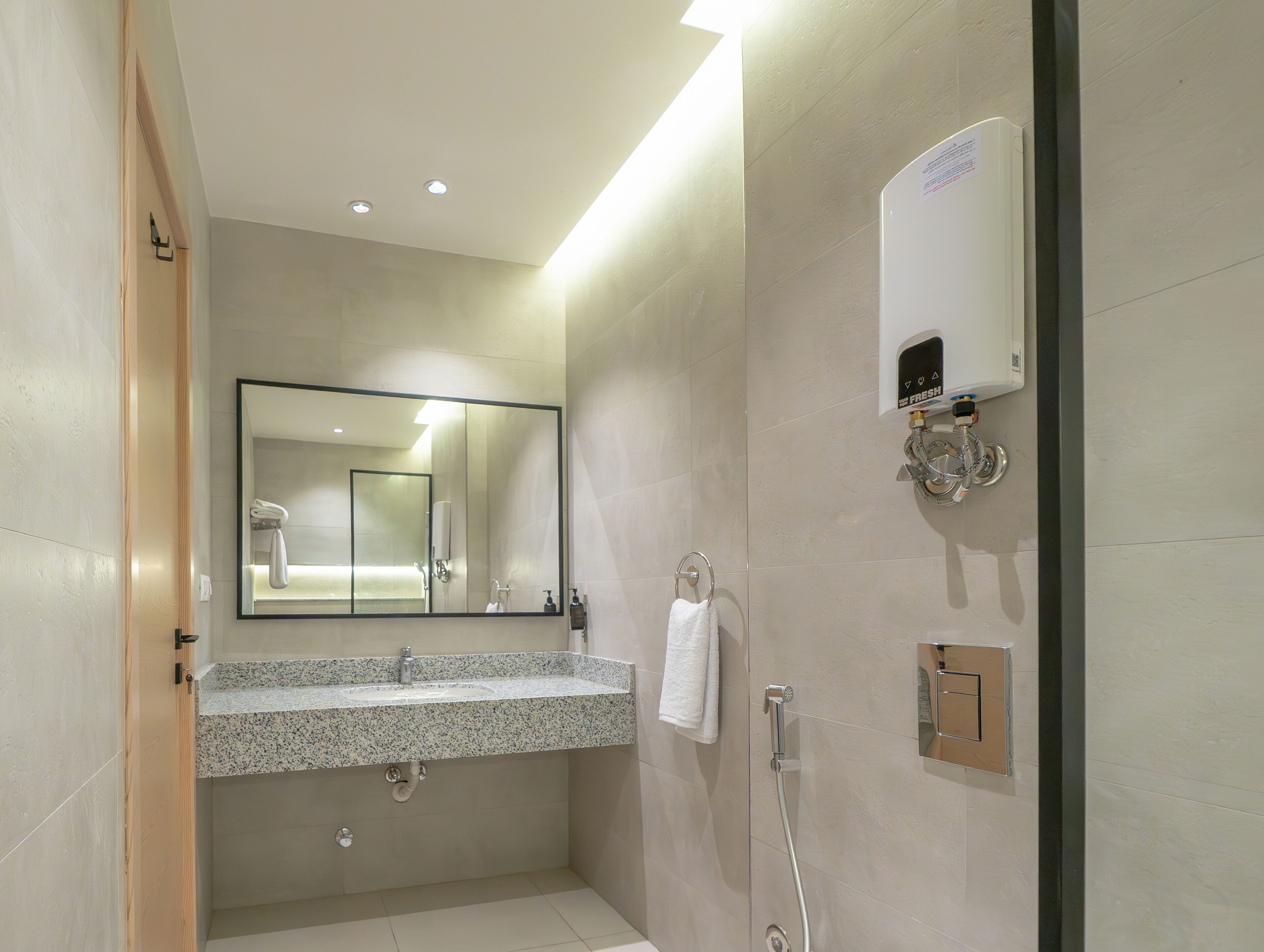 A modern bathroom with a granite countertop sink, a large mirror, a handheld showerhead, and a wall-mounted soap dispenser.