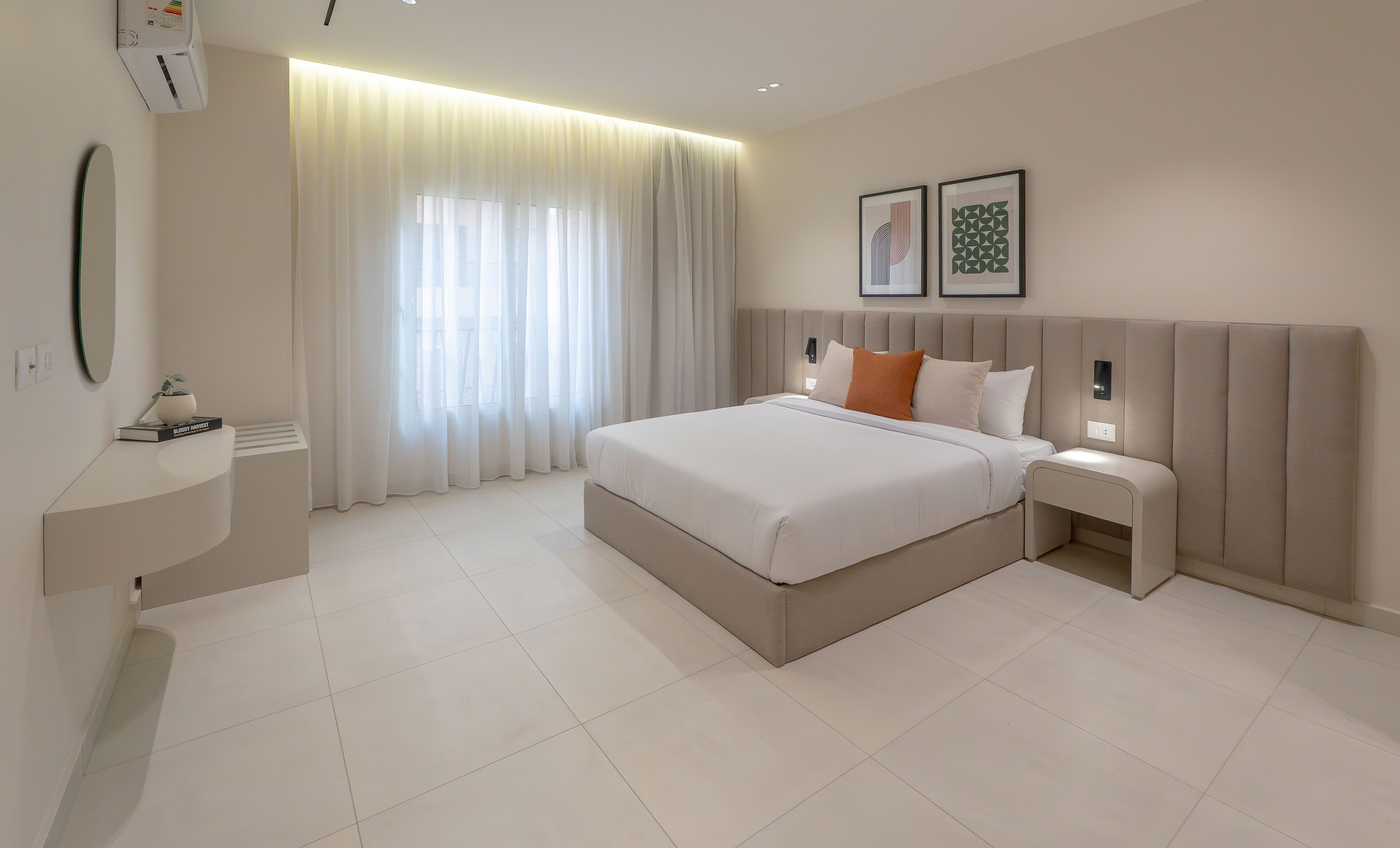 Quarto de hotel moderno com uma cama grande, mesas de cabeceira, um espelho e uma janela com cortinas.