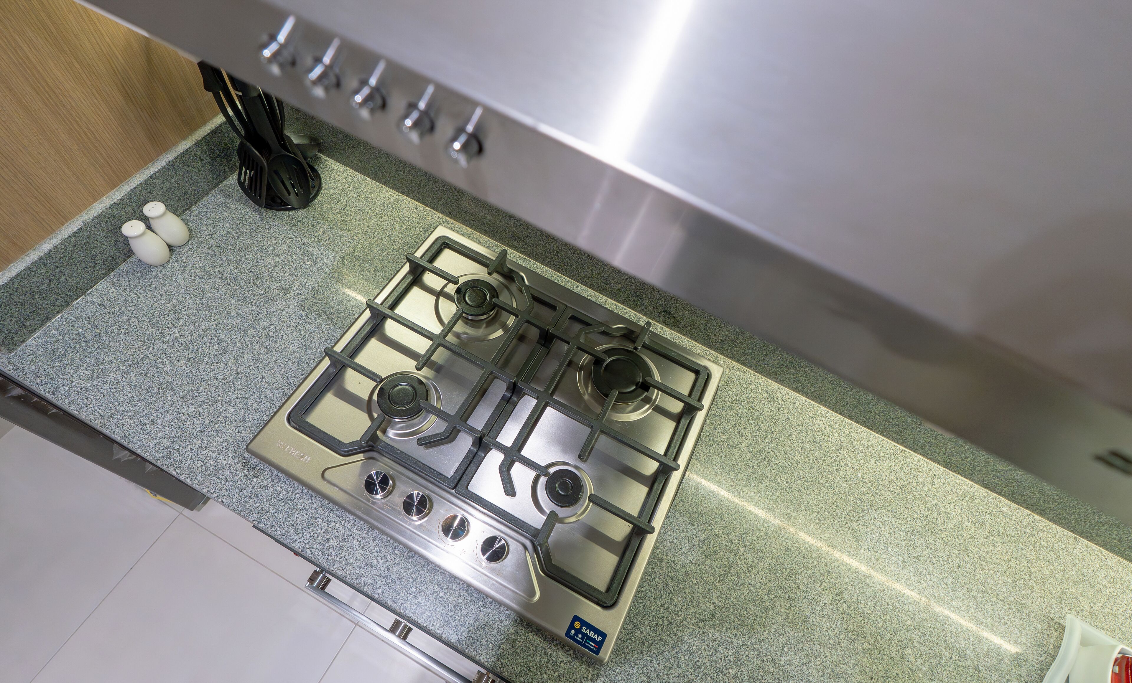 A kitchen with a stainless steel gas stove, a granite countertop, and a stainless steel range hood.