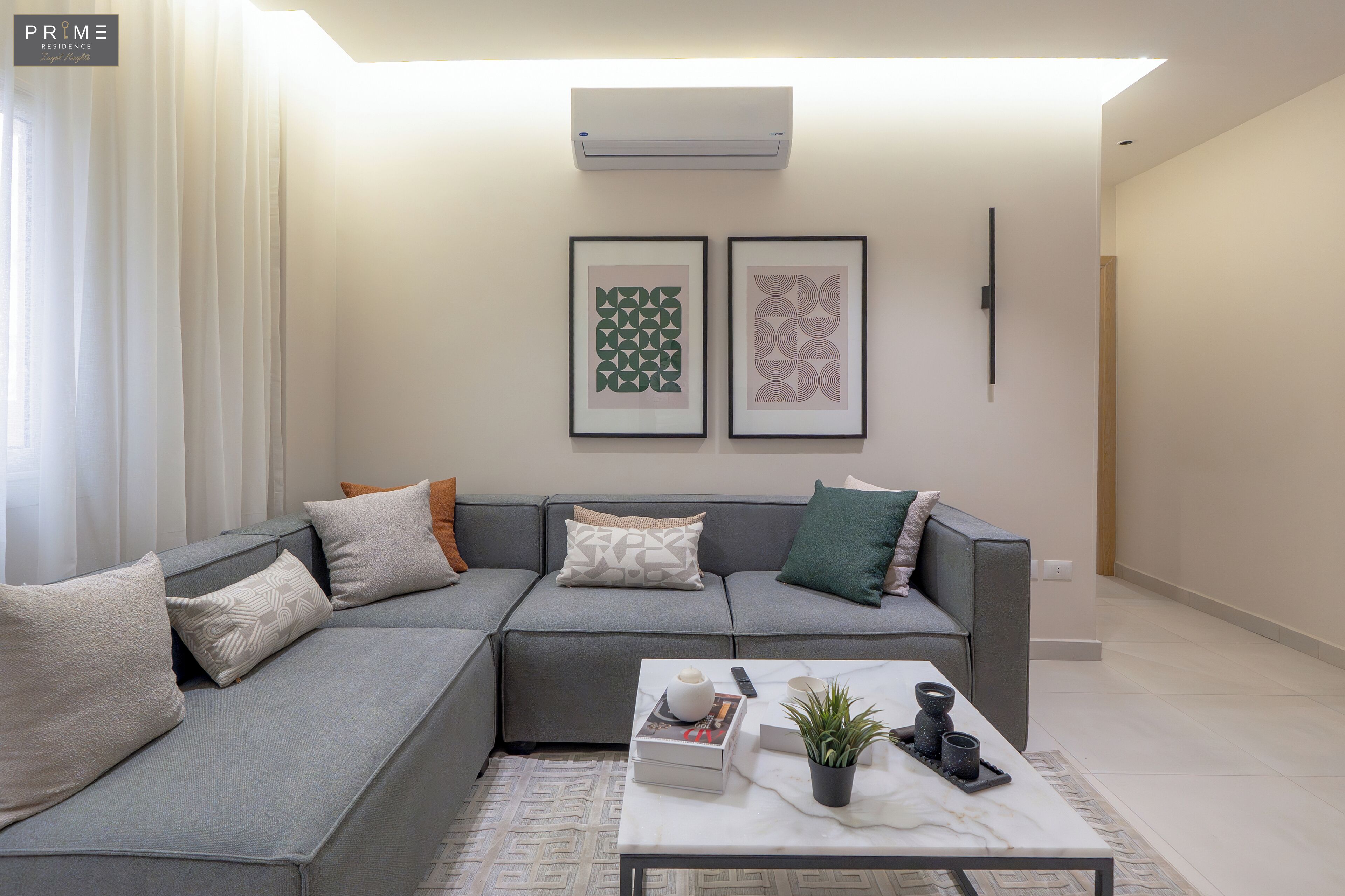 A modern living room with a sectional sofa, a coffee table with decorative items, and two framed artworks on the wall.