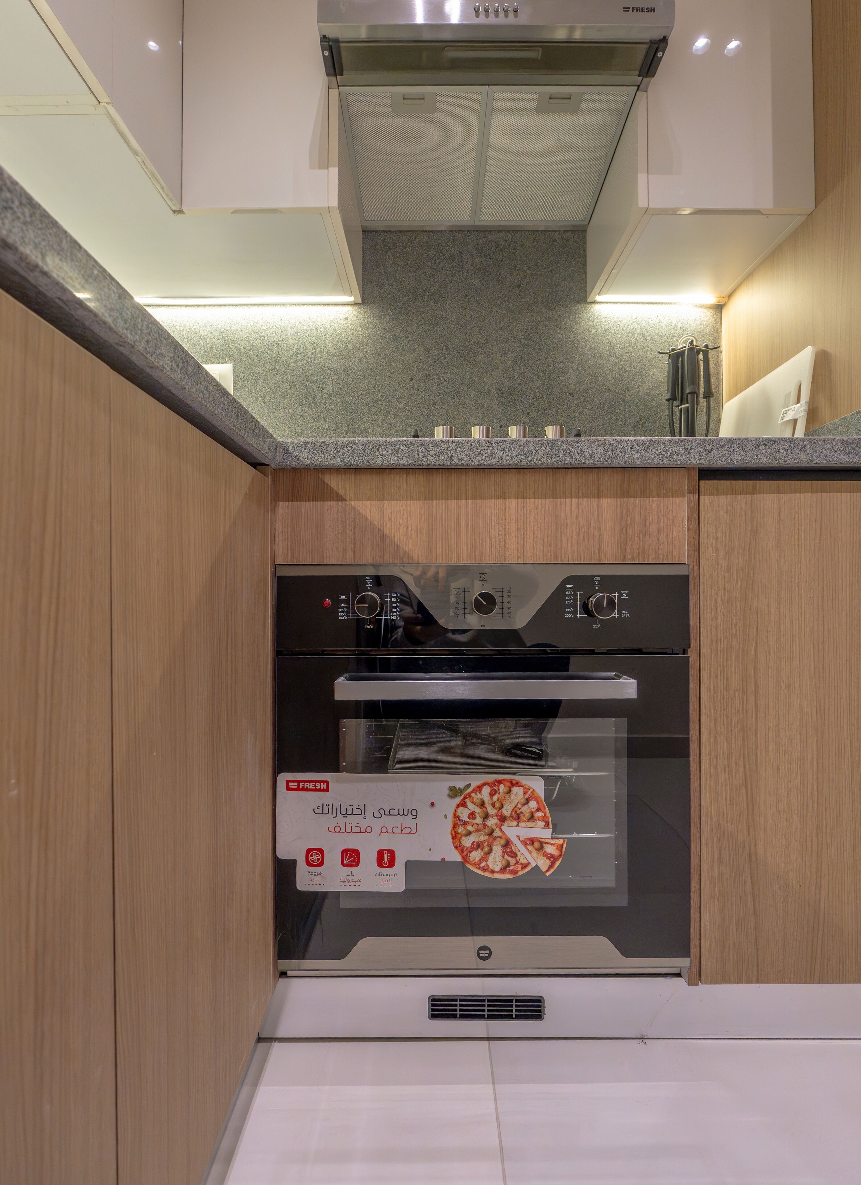 Una cucina con forno integrato, cappa aspirante in acciaio inox e mobili in legno.