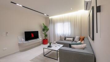 A modern living room with a flat-screen TV, a sofa, a coffee table, and a potted plant.