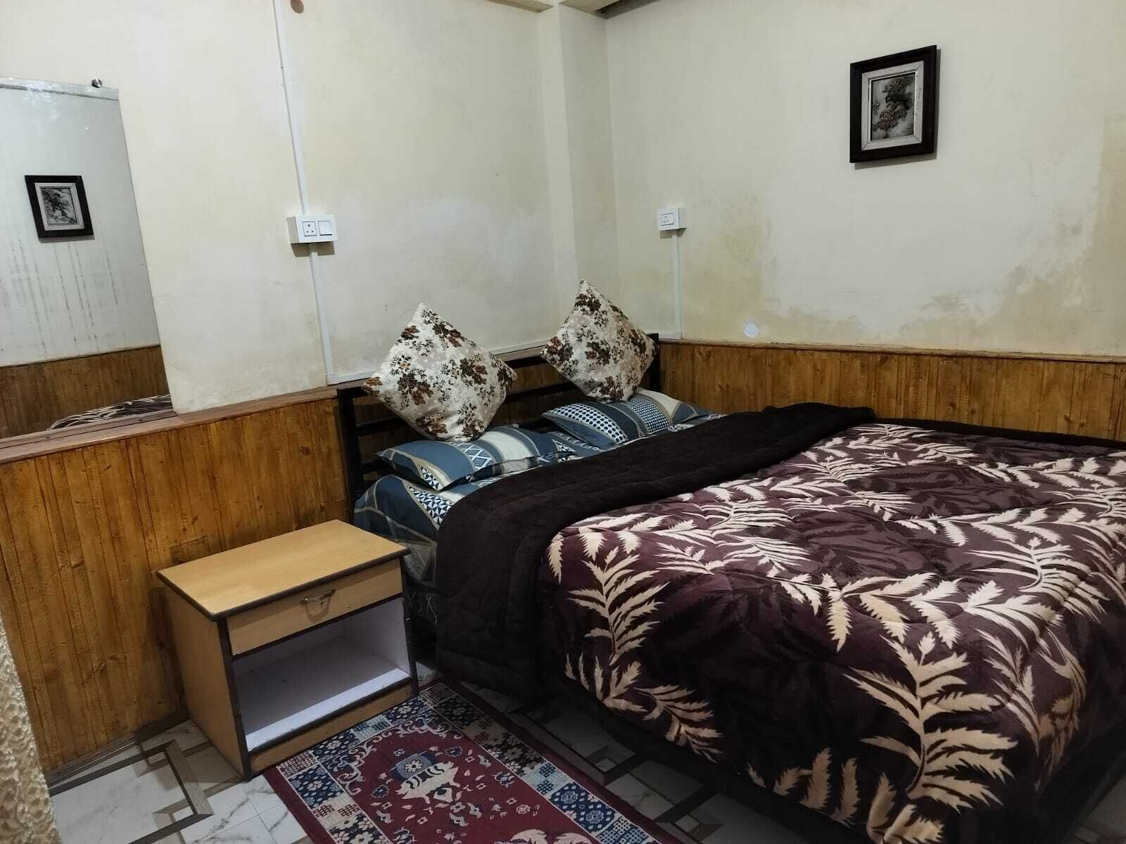 A bedroom with a wooden headboard, a bed with patterned bedding, a small bedside table, and a rug.