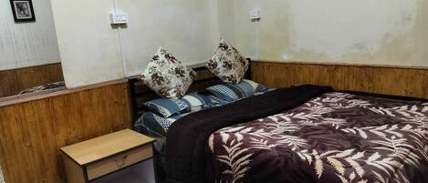 A bedroom with a wooden headboard, a bed with patterned bedding, a small bedside table, and a rug.