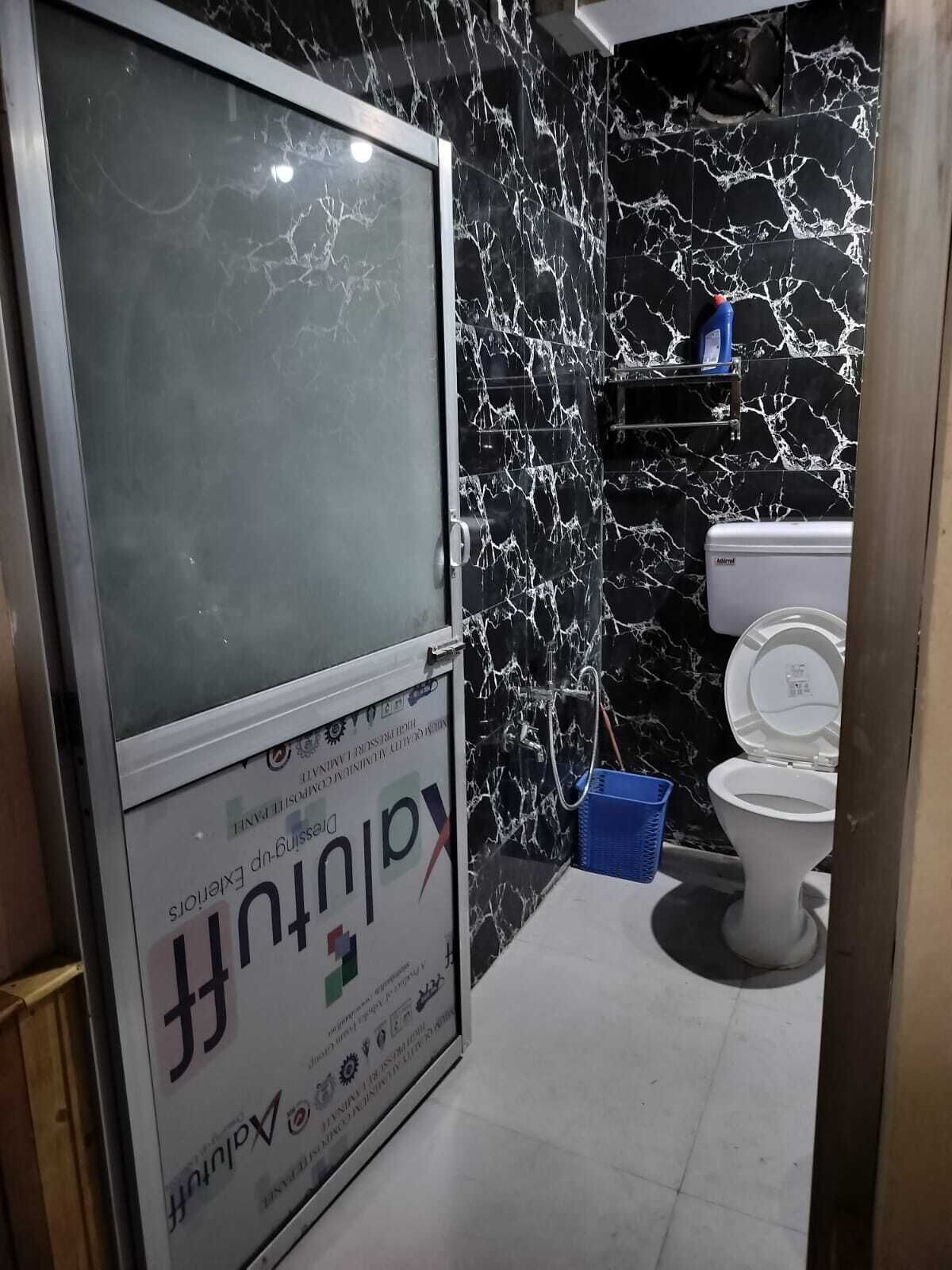 A bathroom with a black marble wall, a white toilet, and a glass door with a sign.