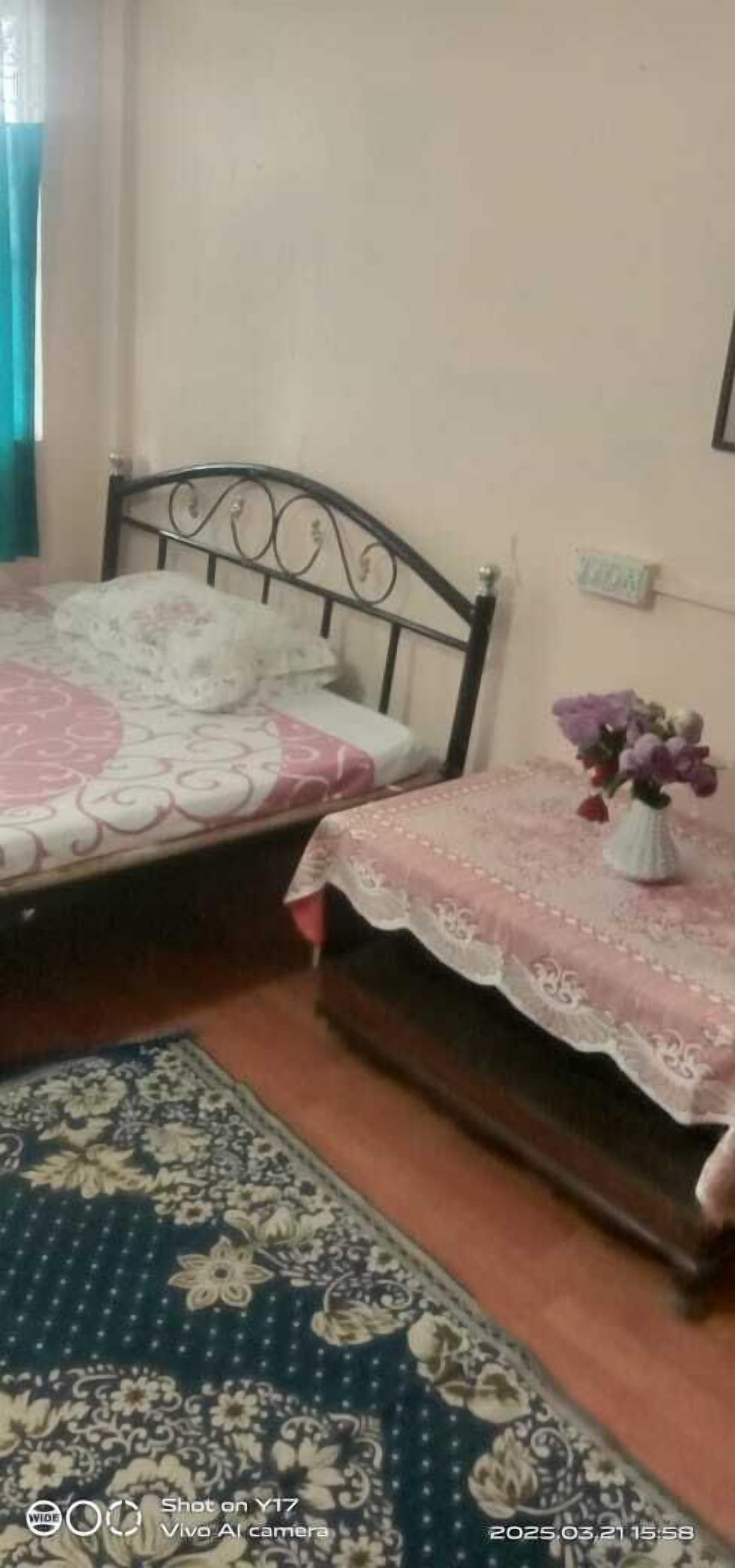 Un dormitorio con dos camas, un tapete estampado y un jarrón con flores.