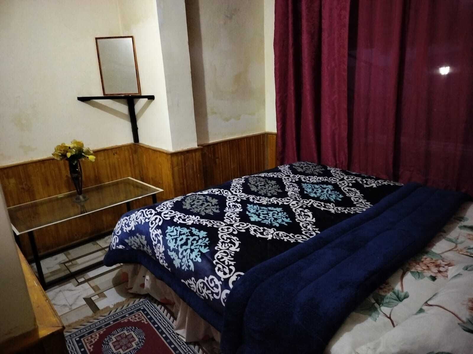 Quarto com cama, mesa de cabeceira, espelho e janela com cortinas.