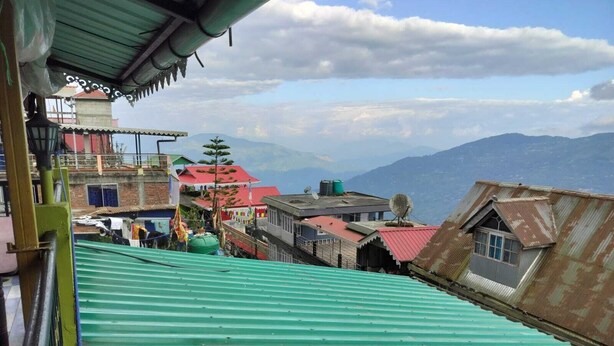 A view of a hillside with buildings, including a green-roofed structure and a red-roofed building with a satellite dish. - benus (Darjeeling)