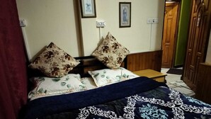 A bedroom with a bed, floral pillows, a patterned bedspread, a nightstand, and a wooden door. - benus (Darjeeling)