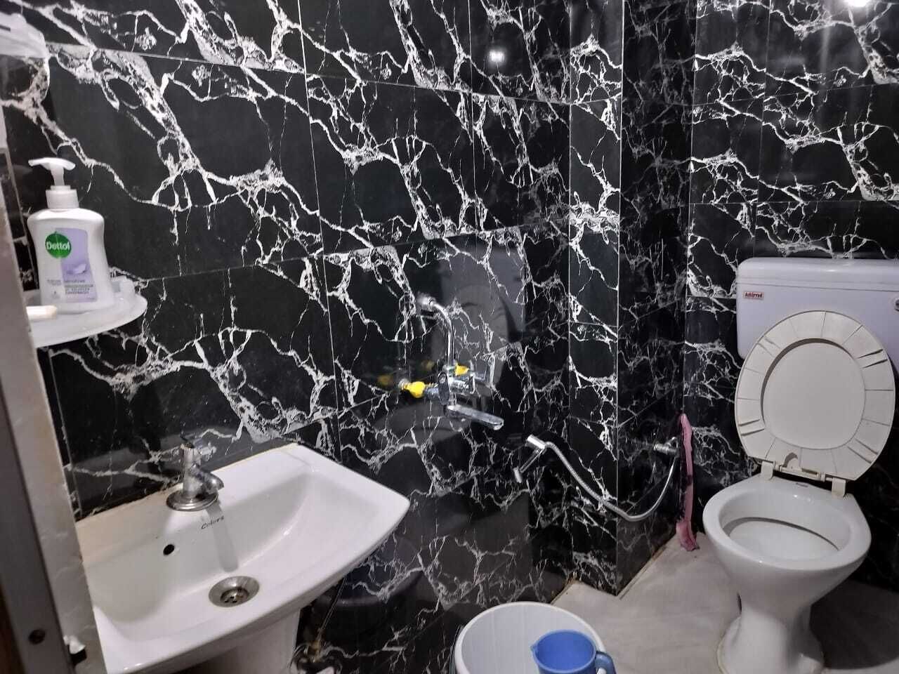 Un baño con pared de mármol negro, un lavamanos blanco y un inodoro.
