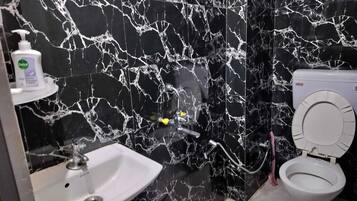 Un baño con pared de mármol negro, un lavamanos blanco y un inodoro.