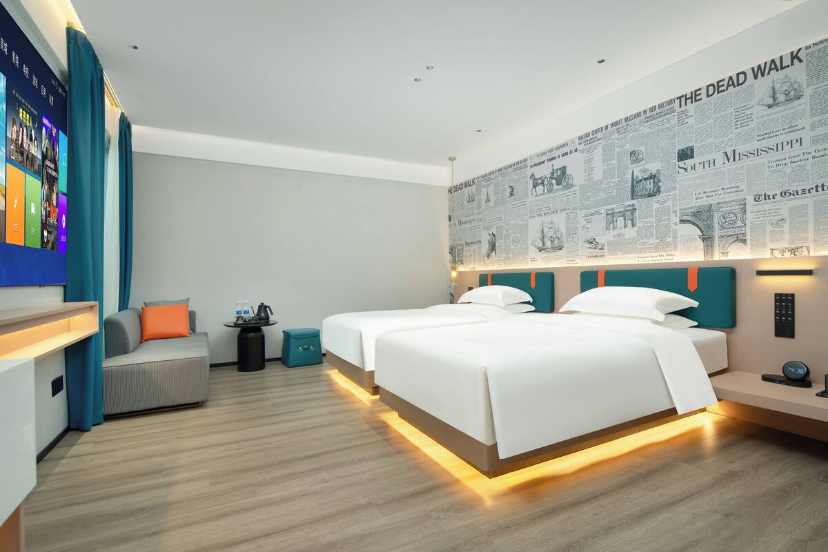 A modern hotel room with two beds, a flat-screen TV, and a wall with newspaper clippings.
