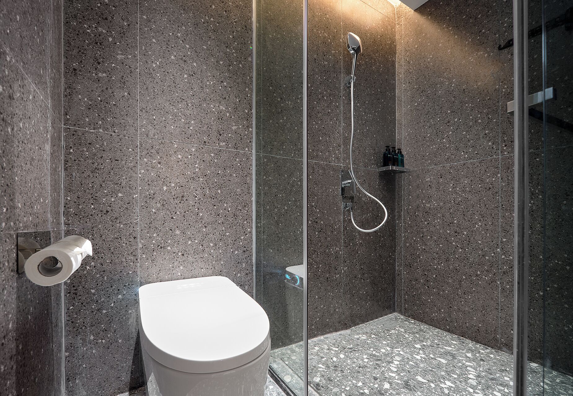 A modern bathroom with a glass-enclosed shower, a white toilet, and a marble floor.